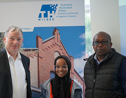 Prof. Michael Herzog und Prof. James Wakiru und eine kenianische Teilnehmerin vor einem Th Wildau-Schild