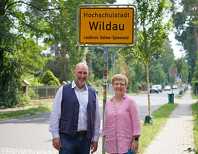 Wildaus Bürgermeister Frank Nerlich und TH-Wildau-Präsidentin Prof. Ulrike Tippe vor einem Ortseingangsschild der Hochschulstadt Wildau