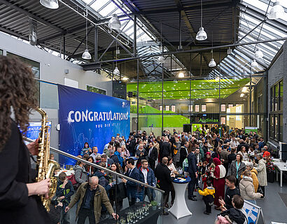 Blick von oben auf das mit Menschen gefüllte Audimax-Foyer und im Vordergrund steht Saxophonistin und spielt