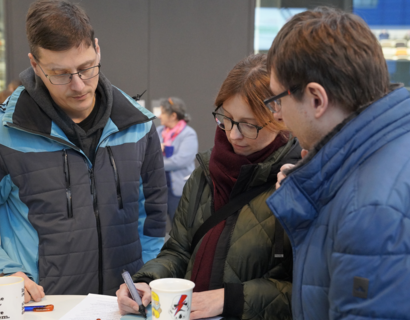 Drei Menschen stehen an einem Tisch und eine Person schreibt