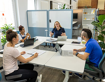 Opp:Lab Eine Professorin und drei Studierende sitzen an einem Tisch und diskutieren.