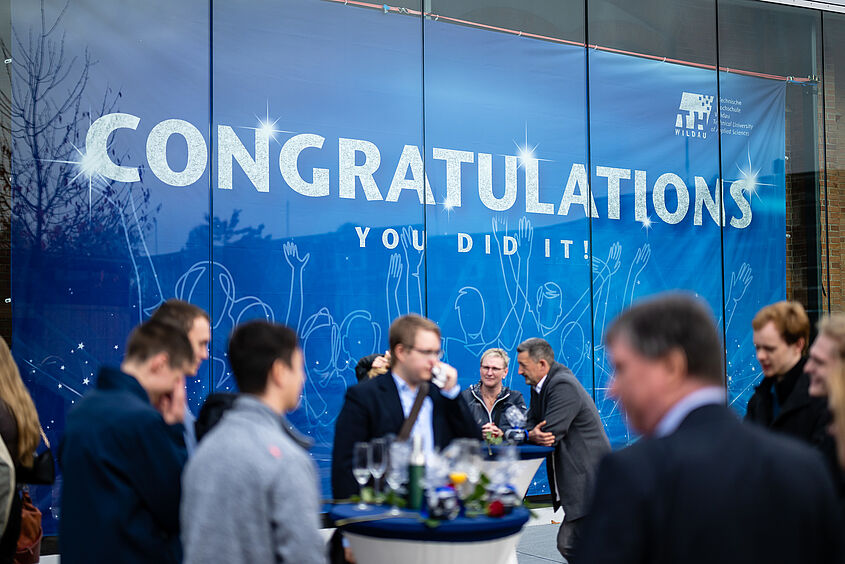 Absolventinnen und Absolventen vor dem Banner in Halle 17 bei der Verabschiedung 2022