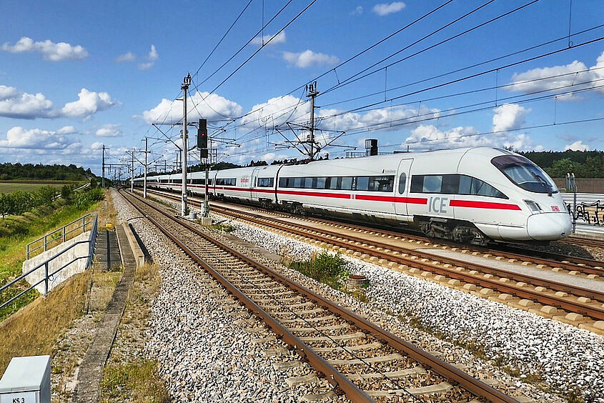 ICE Zug fährt auf einer Bahnstrecke durch die Landschaft.