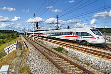 ICE Zug fährt auf einer Bahnstrecke durch die Landschaft.