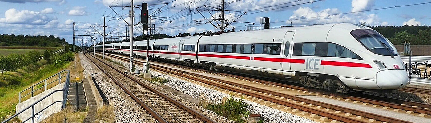 ICE Zug fährt auf einer Bahnstrecke durch die Landschaft.