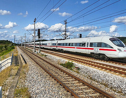 ICE Zug fährt auf einer Bahnstrecke durch die Landschaft.