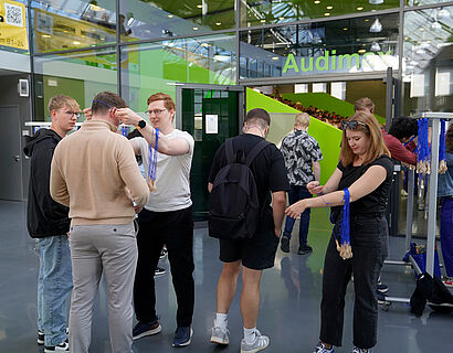 Studierende im Foyer eines Hörsaalgebäudes bekommen ihren Erstsemester-Löffel umgehängt