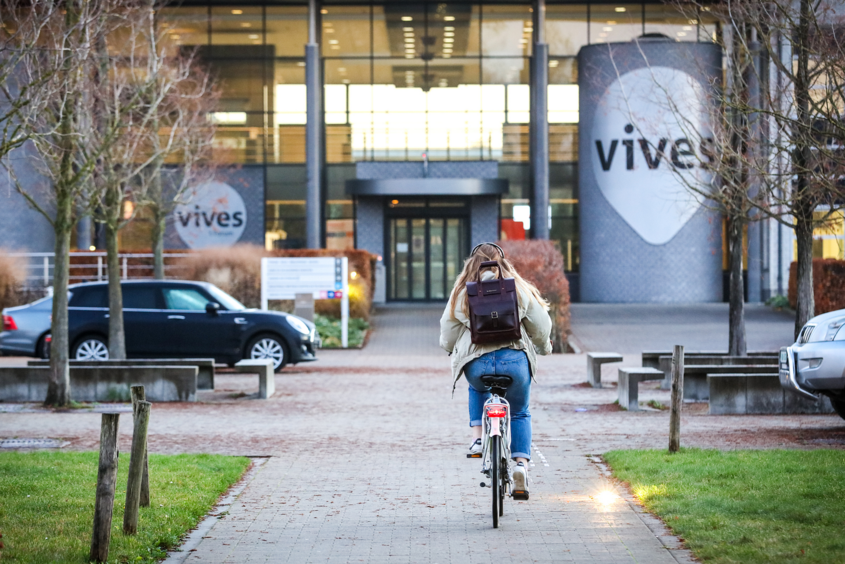 Studierende mit dem Rad auf dem Weg zur VIVE Hogeschool (im Hintergund)