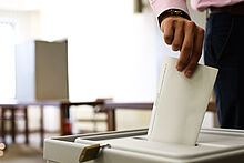Person steckt Zettel in Wahlurne