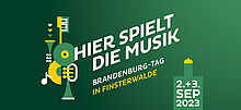 Slogan "Hier spielt die Musik" in weiß auf grünem Hintergrund mit Datum des 17. Brandenburg-Tages in Finsterwalde