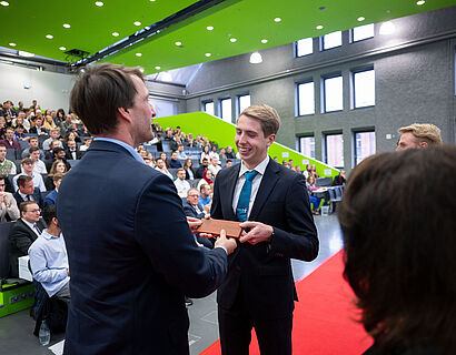 Prof. Rainer Stollhoff der TH Wildau übergibt einem Absolventen einen roten Klinkerstein mit der Aufschrift "Best Student"