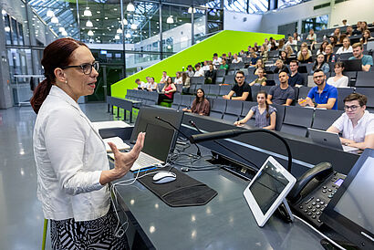 Profilansicht einer Professorin, die in einem vollen Hörsaal eine Vorlesung hält.