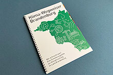 Broschüre mit der Aufschrift "Klimawegweiser Brandenburg" auf einem türkisfarbenen Hocker