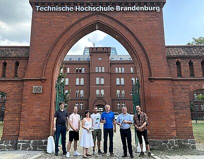 Zum Kick-Off-Meeting fand sich das hochschulübergreifende FASER-Projektteam an der Technischen Hochschule Brandenburg zusammen. Leute aus dem Projekt stehen vor einem Eingangstor der TH Brandenburg