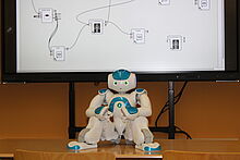 Humanoider Roboter auf Tisch vor einem Bildschirm